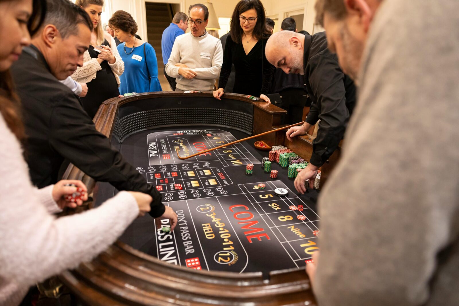 Group of adults playing craps around a casino table, engaging in betting and socializing.